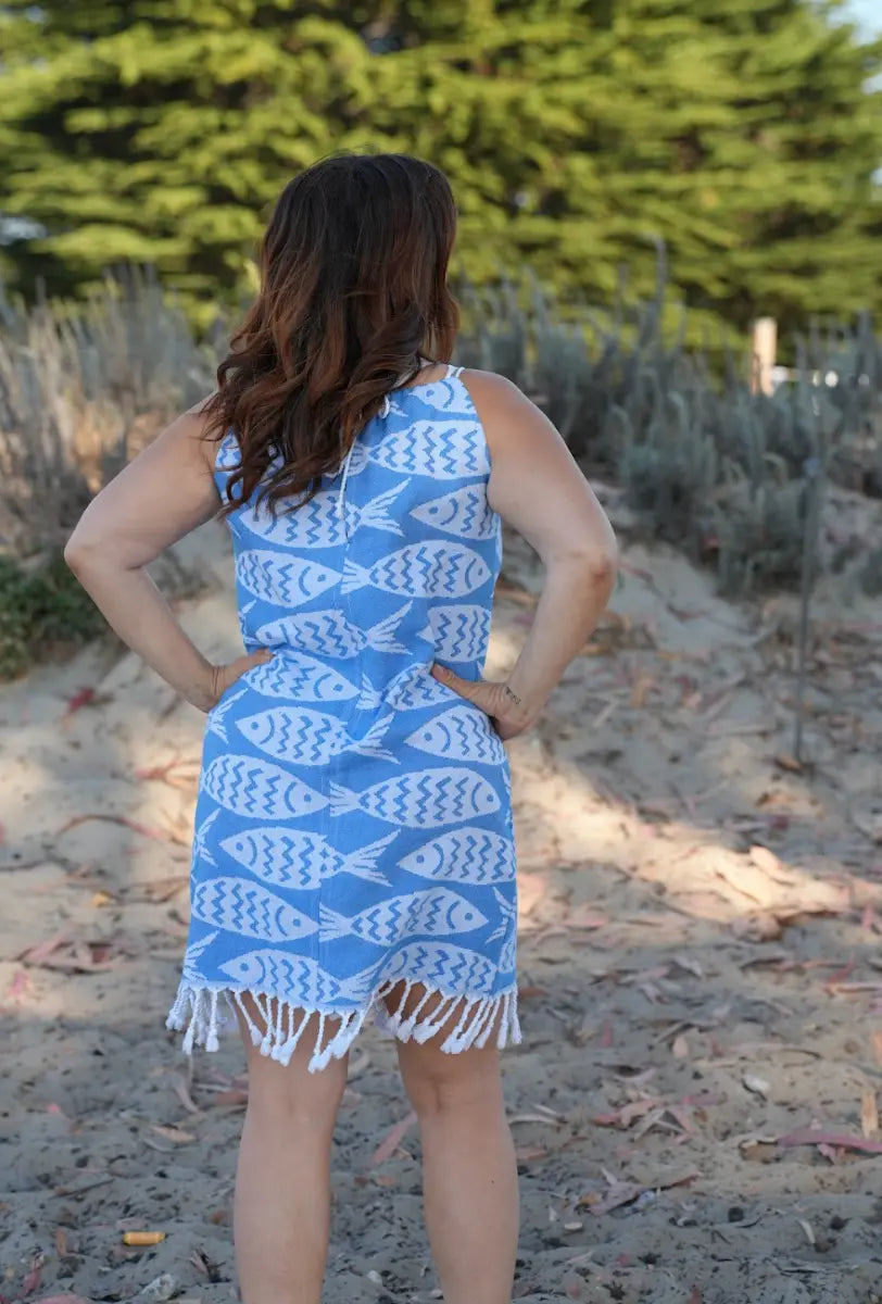 Woman wearing a blue dress with white fish pattern on a sandy beach.