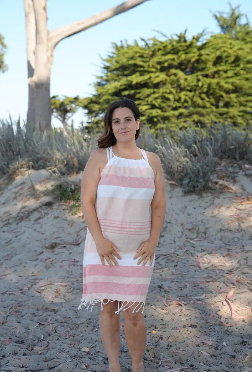 Woman on beach wearing a sleeveless peach, salmon and white striped cover-up  with tassels