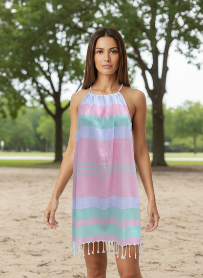 Woman wearing a pink, green and white striped dress on a sandy beach with trees in the background