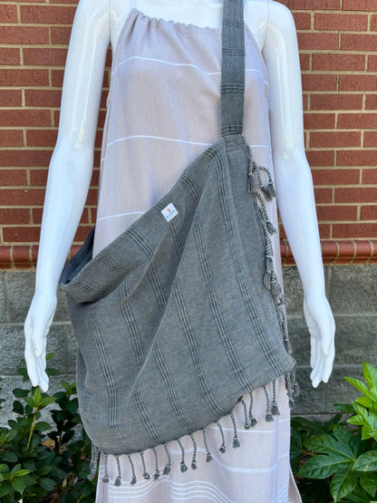 Gray bag with tassels on a mannequin wearing a tan maxi dress against a brick wall