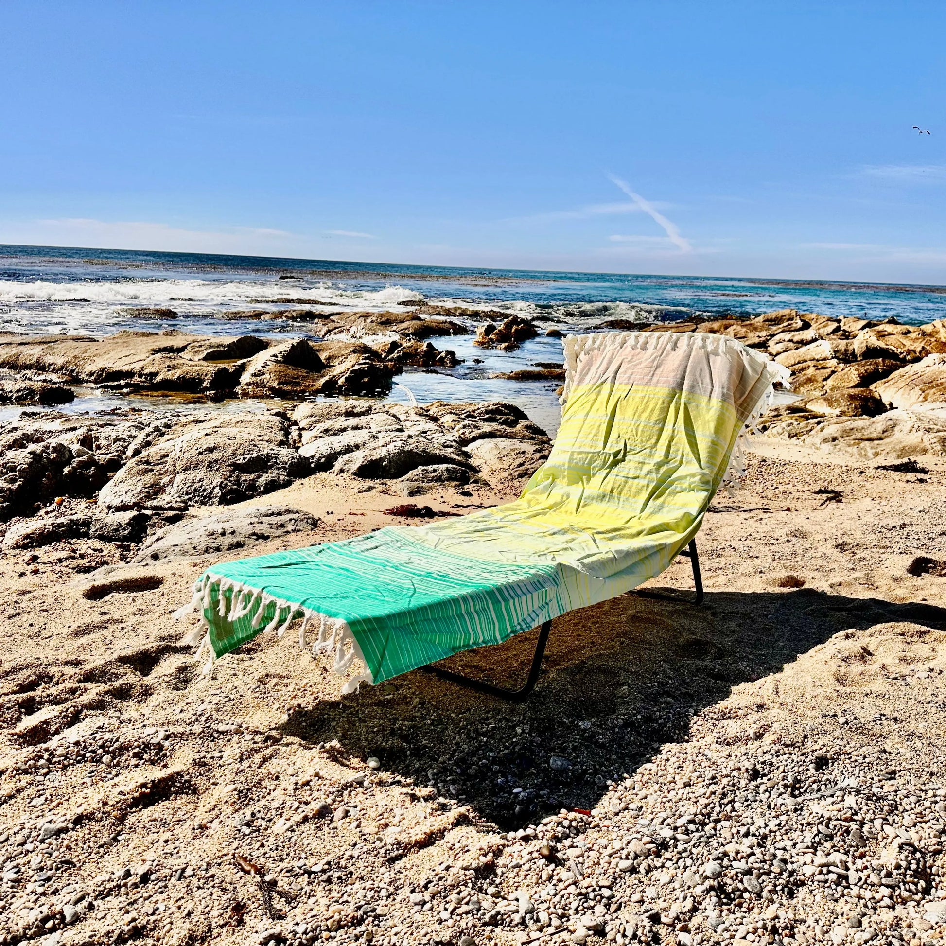 Beach chair with a colorful towel draped over it on a rocky beach.