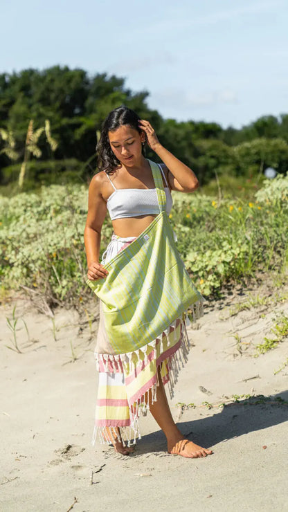 Woman on a beach wearing a colorful sarong carrying a green bag
