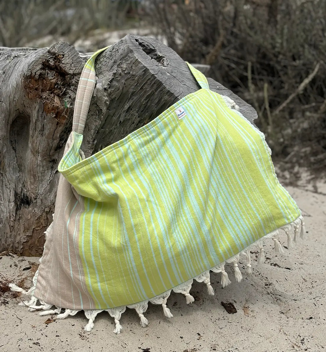 Green and beige striped bag with tassels on a sandy background