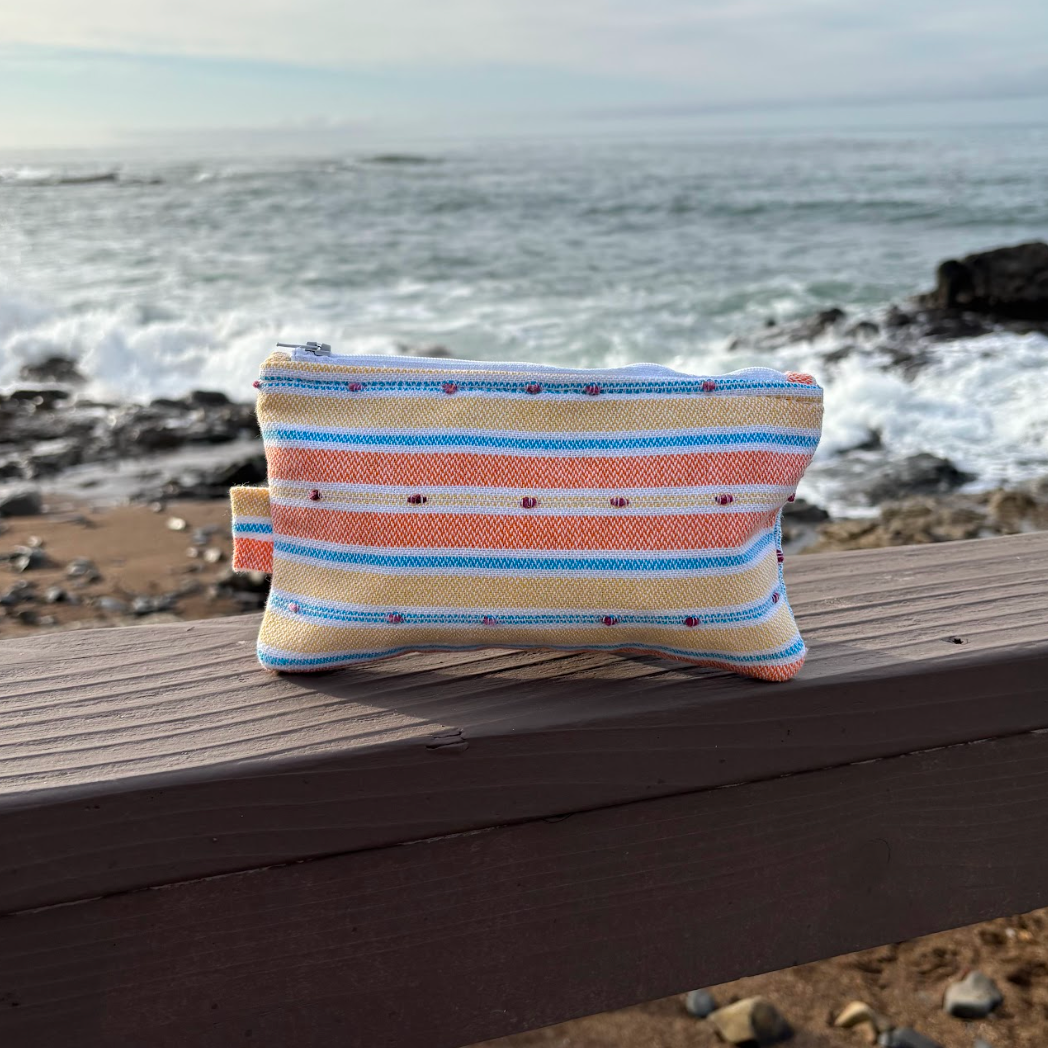 A small orange and yellow striped makeup bag placed on a wooden surface with a beach background.