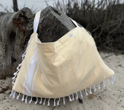 Yellow tote bag with white fringe on a sandy background