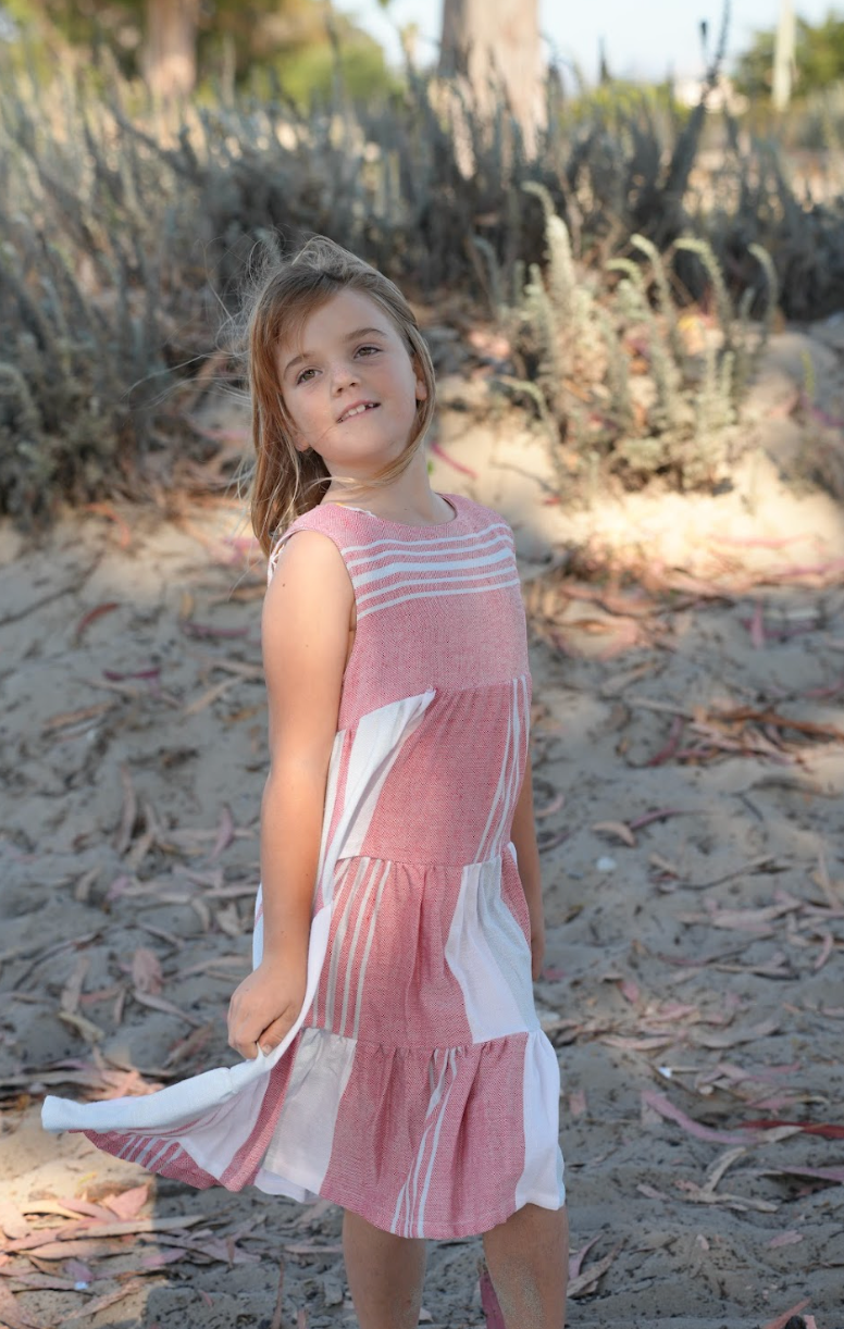 Young girl wearing a three-tiered red, blue and white striped sleeveless dress with tassels on beach