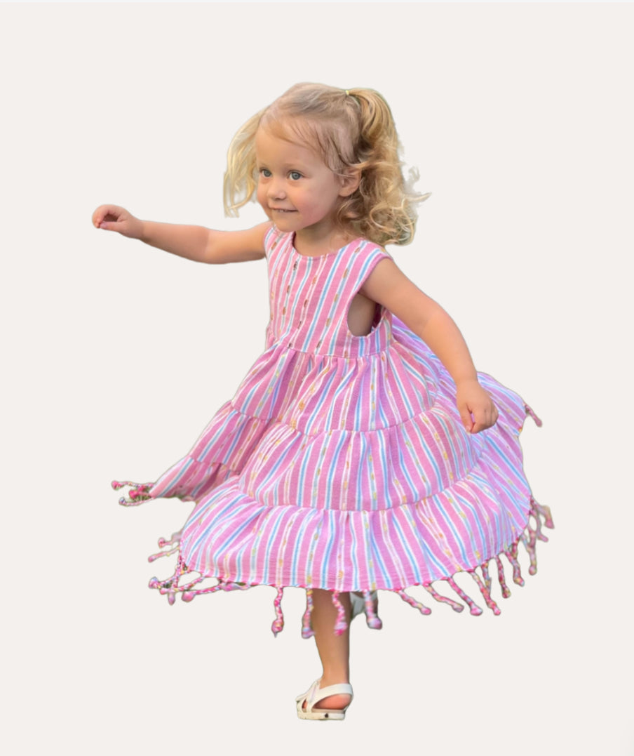Young girl twirling in a three-tiered pink striped sleeveless dress with tassels 
