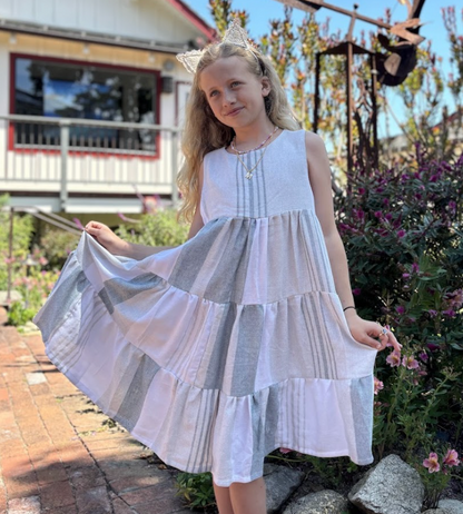 Young girl wearing a three-tiered grey, charcoal and white striped sleeveless dress with tassels outdoors