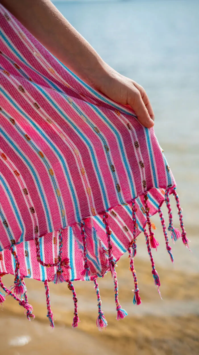 Close-up of a pink striped dress hem with tassels on a beach.